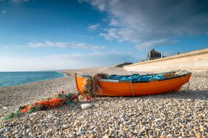 chesil beach - attractive pebble beach with orange fishing boat in the foreground and strikingly blue ocean in the background