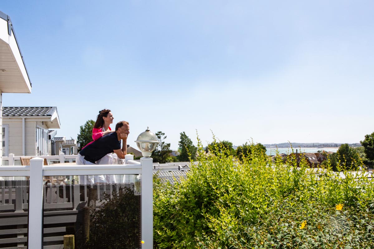 A couple on the balcony of a caravan looking out towards the sea
