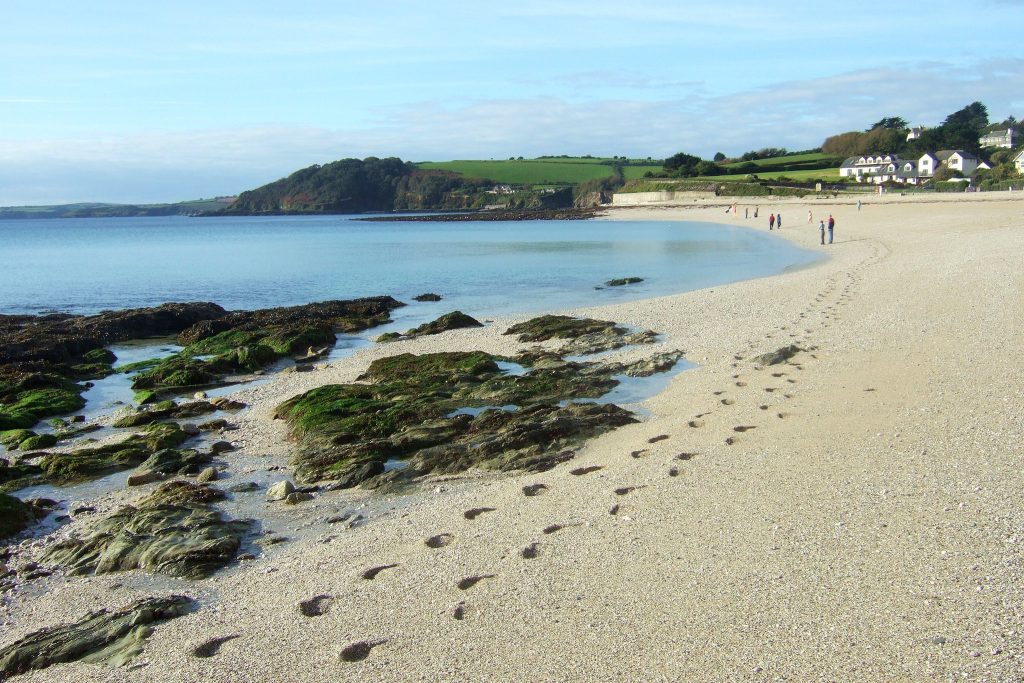 Attractive shingle beach with seaweed and footprints along the edge of the coast. Blue sea and cloudless sky