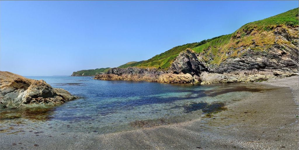 Gorgeous beach with clear water against a green hilly background and cloudless sky