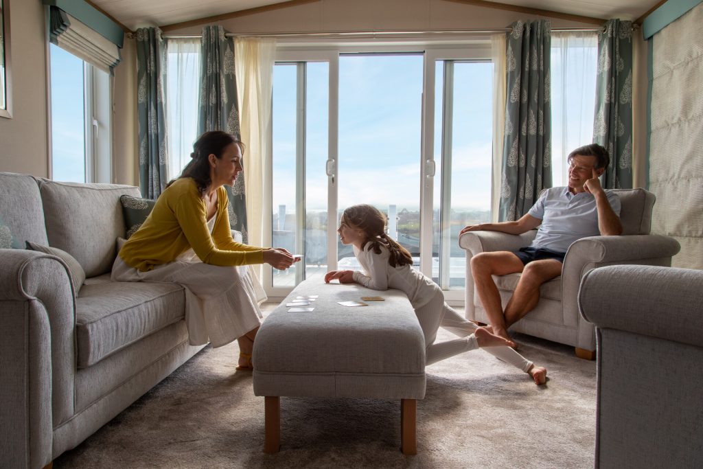 Scene of a family of three with young daughter enjoying quality time in a cosy living room with floor to ceiling windows overlooking a sea view